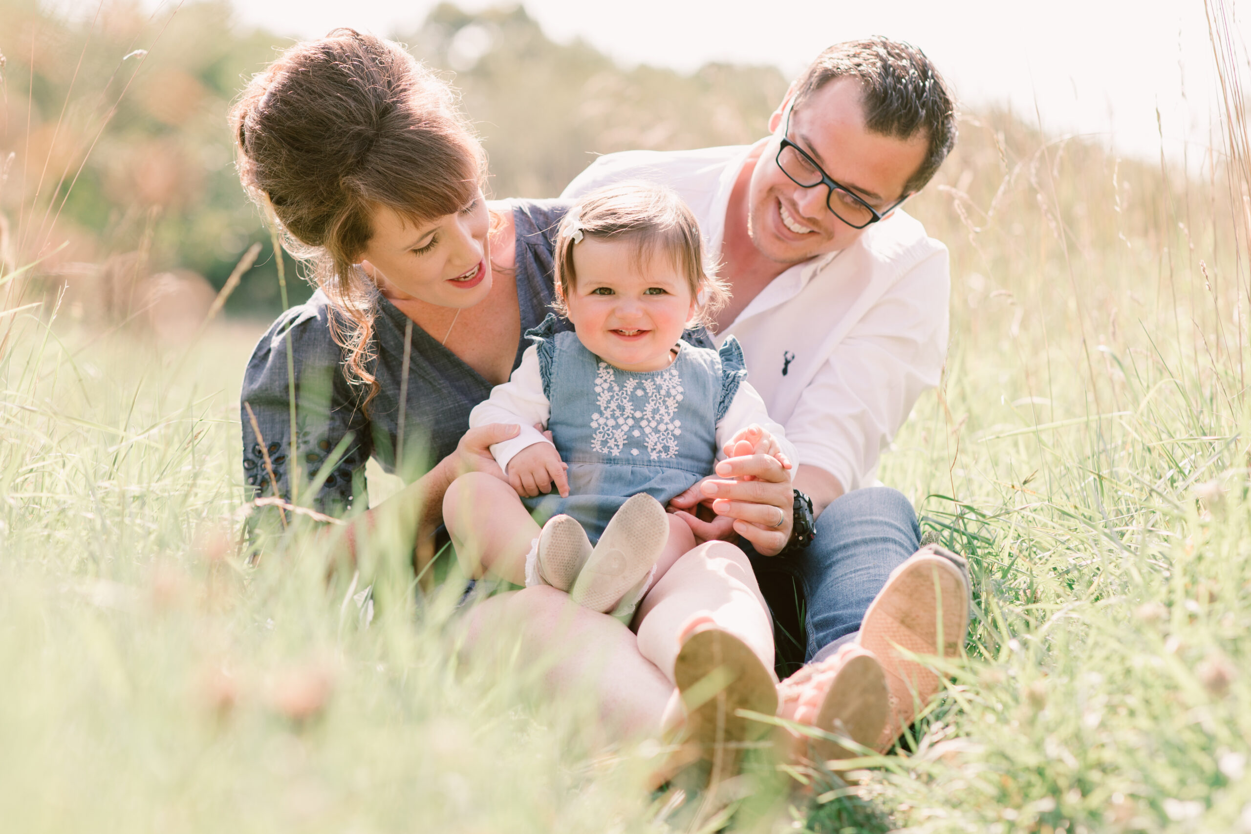 Family Photographer in Hampshire | Young family sat in the grass at Warsash Common, smiling at their toddler