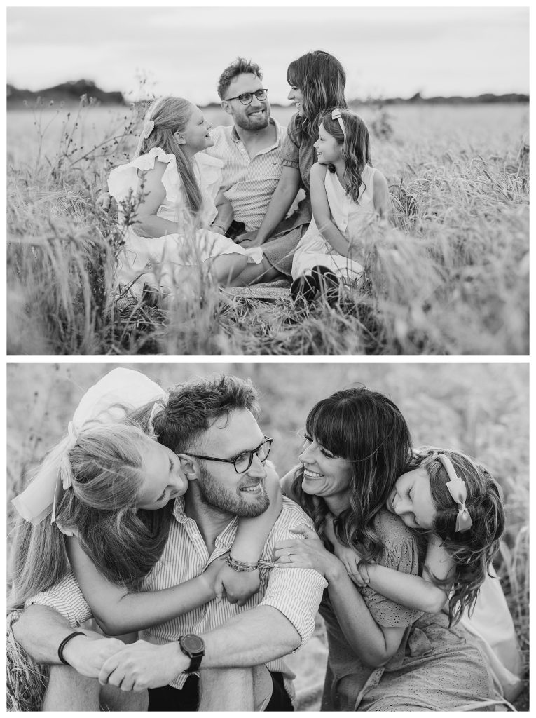 golden hour family shoot in Hampshire with Hampshire Photographer Lucylou Photography captures a natural golden hour moment of a blended family sitting in a barley field. Parents Elliott and Chantelle sit close, smiling at each other, while their daughters lean in with hugs and laughter in soft evening light. Photos are in black and white