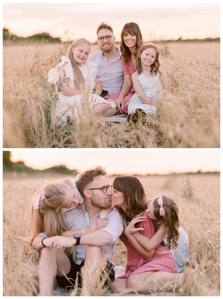 golden hour family shoot in Hampshire with Hampshire Photographer Lucylou Photography captures a natural golden hour moment of a blended family sitting in a wheat field at Meon Shore. Parents Elliott and Chantelle sit close, kissing each other, while their daughters lean in with hugs and laughter in soft evening light