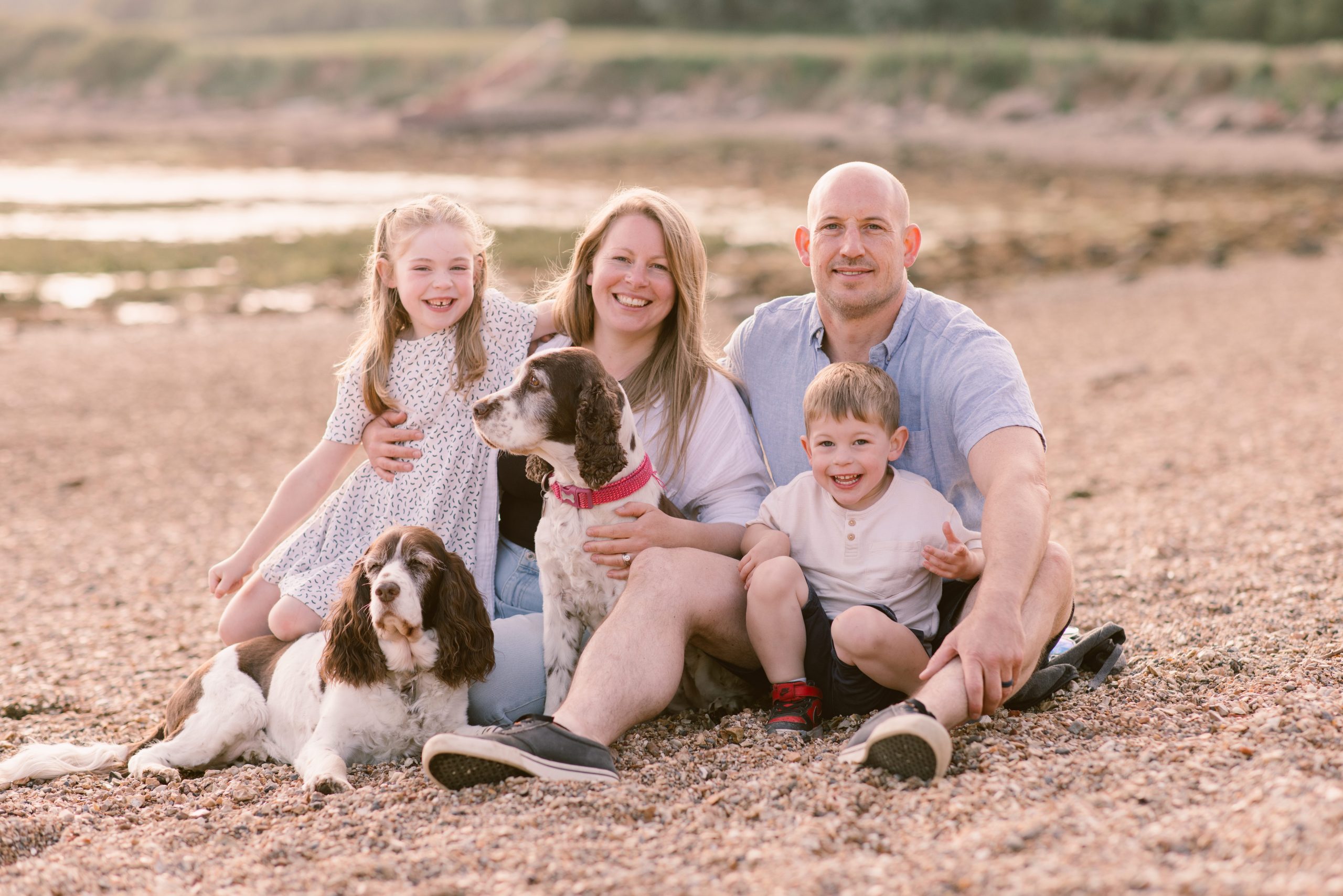 Professional Family Photos on the beach - parents holding young children and dogs all smiling at the camera
