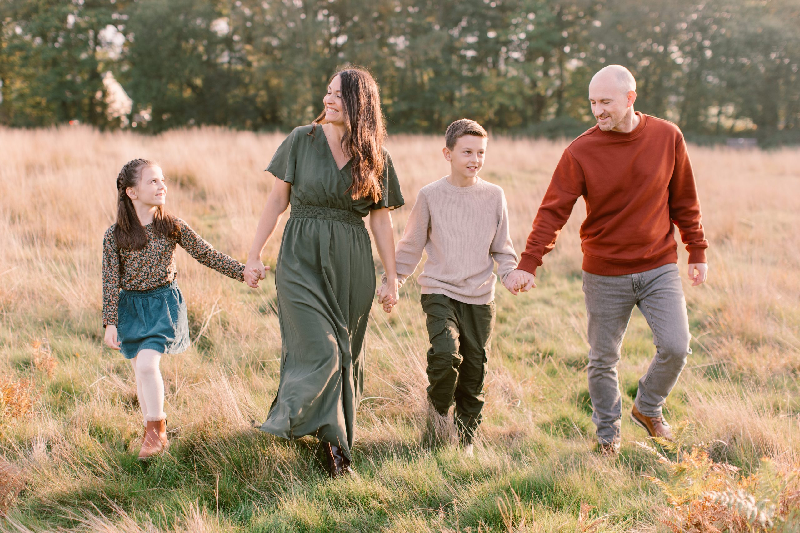 Family walking together, holding hands and looking at each other with smiles on their faces - Hampshire Family Photographer 